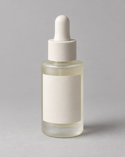 Frosted glass serum bottle with a blank cream label and ivory dropper cap on a soft gray studio background.