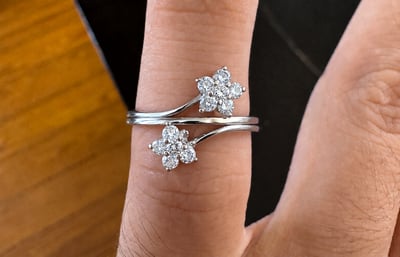 Silver-tone ring on a finger with a continuous central band, two offset floral clusters, and curved connecting stems