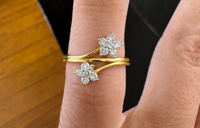 Yellow-gold-tone ring on a finger with two offset floral clusters of clear stones and a continuous central band