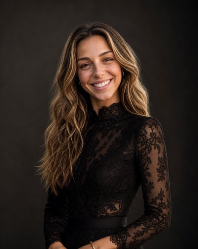 Adult woman with wavy light-brown hair in a high-neck black floral lace dress and gold jewelry against a dark studio background