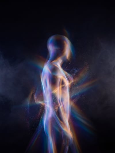 Glowing veiled human figure dissolving into blue, orange, and violet light trails on a dark background.